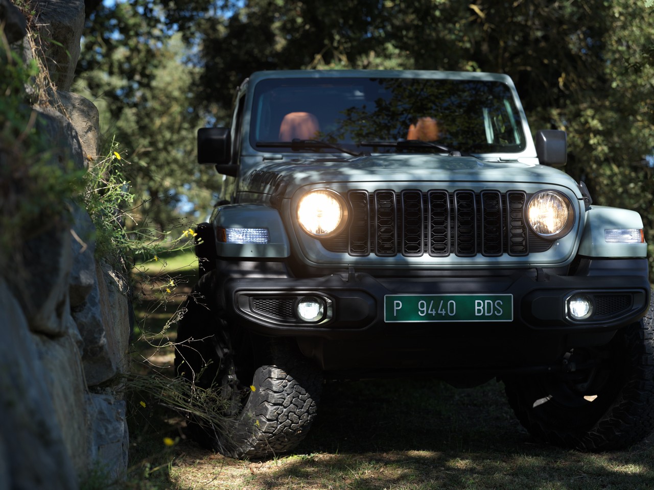 El frente de un Jeep Wrangler Rubicon entre los árboles, con los faros encendidos